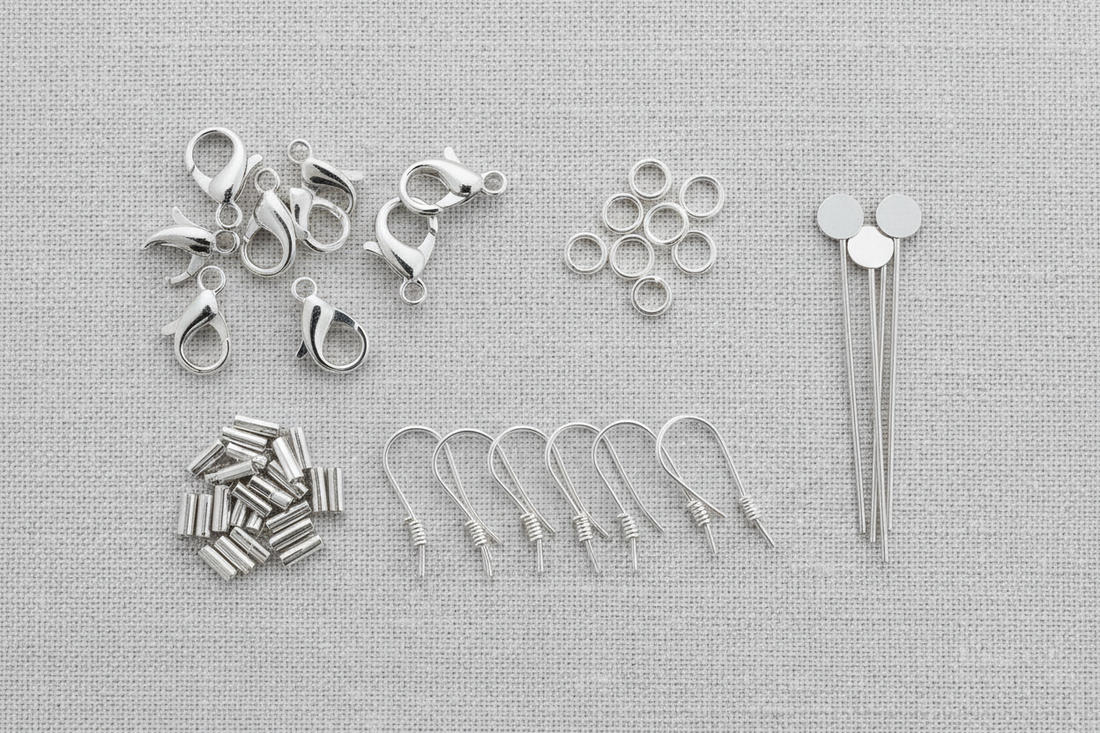"Assorted sterling silver jewelry findings including lobster claw clasps, jump rings, ear wires, crimp tubes, and head pins arranged on a linen texture background"